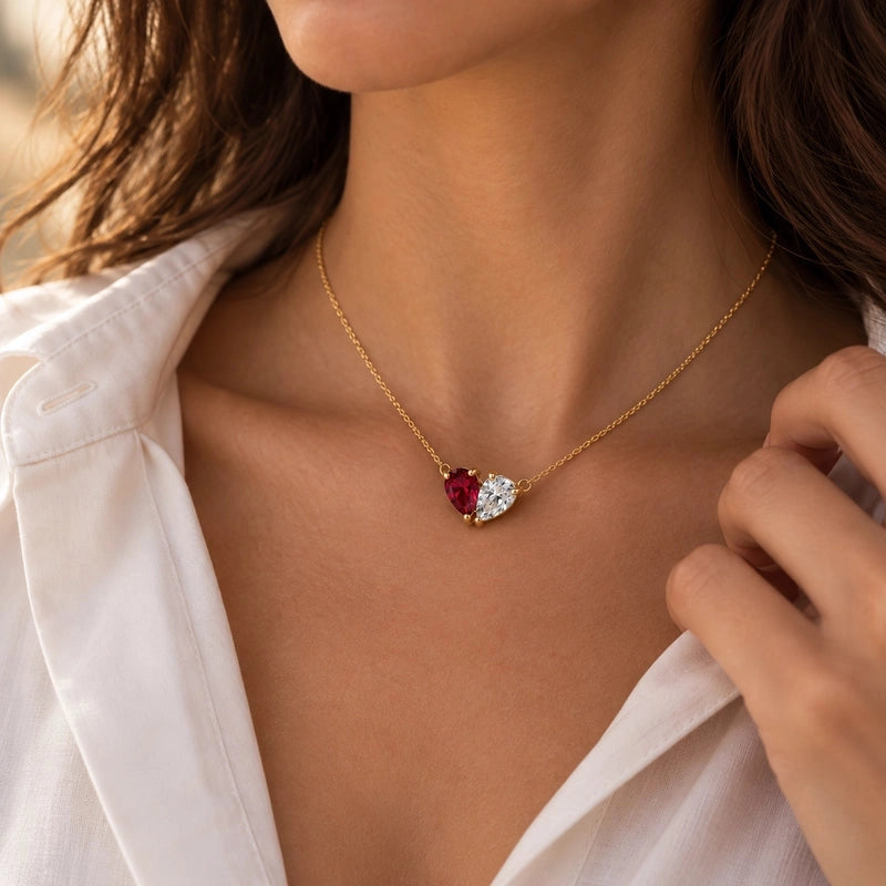 Gold Elara necklace with red and clear heart-shaped birthstones, worn close to the heart